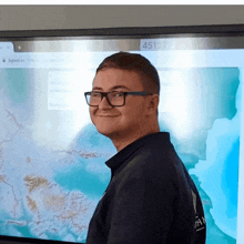 a man wearing glasses stands in front of a monitor that says 451273