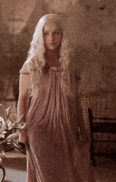 a woman in a long pink dress is standing in front of a chair