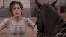 a woman in a white dress is standing next to a black horse in a field .