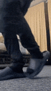 a person wearing black pants and black slippers is standing on a carpet