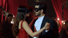 a woman in a red dress and mask is dancing with a man