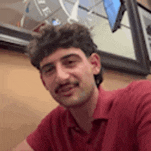 a man with a mustache is wearing a red shirt .