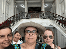 three women pose for a picture in front of a large staircase