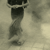 a woman in a long black dress is walking through a foggy area