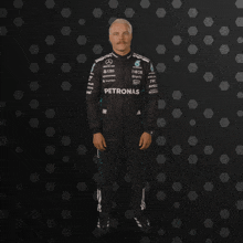 a man in a petronas racing suit stands in front of a black background