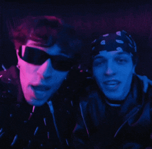 a man wearing sunglasses and a bandana stands next to another man wearing sunglasses