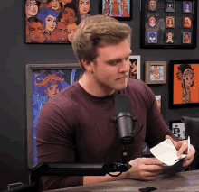 a man sitting in front of a microphone holding a piece of paper with a picture of a woman on the wall behind him