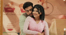 a man is hugging a woman in a pink sweater in a room .