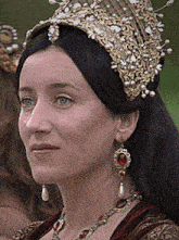 a woman wearing a crown and earrings looks to the side