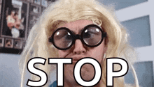 a man wearing glasses and a blonde wig has the word stop on his face .