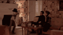 a man in a hat is standing in a living room with a woman and a man sitting on a couch