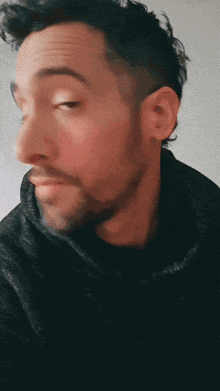a man with a beard wearing a black jacket looks at the camera