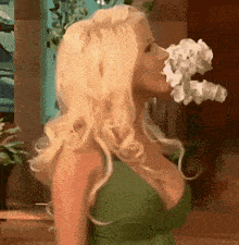 a blonde woman in a green dress is blowing flowers out of her mouth