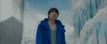 a man in a blue jacket is standing in front of a wall of ice