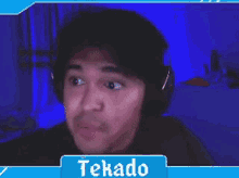 a man wearing headphones is making a funny face in front of a blue screen that says tekado