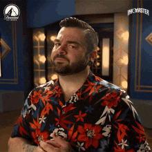 a man in a floral shirt is standing in front of a sign that says ink master