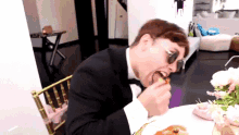 a man in a tuxedo is sitting at a table eating pizza