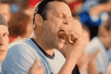 a man in a blue shirt is eating a hot dog in a crowd of people .