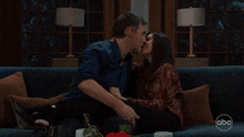 a man and a woman kissing on a couch with abc written on the bottom