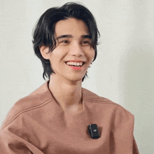a young man with long hair is smiling and wearing a microphone on his neck .