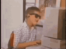 a young boy wearing sunglasses is typing on a computer keyboard .