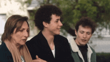 two men and a woman are standing next to each other and the woman is wearing a scarf and the man is wearing a jacket