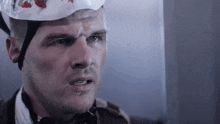 a man wearing a helmet with blood on it and a bandage on his head .