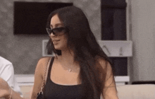 a woman wearing sunglasses and a black tank top is standing next to a man .
