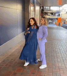 two women are standing next to each other on a sidewalk in front of a building .
