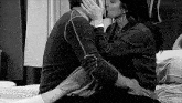 a black and white photo of a man and a woman kissing on a bed .