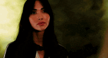 a woman with long black hair is looking at the camera with a serious expression on her face .