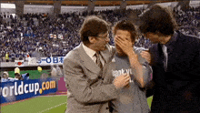 a man covering another man 's face in front of a worldcup.com sign