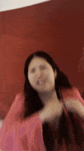 a woman in a pink shirt is dancing in front of a red wall and smiling .