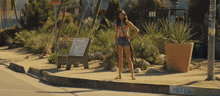 a woman in a bikini stands on a sidewalk next to a sign that says stop