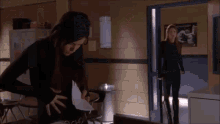 two women are standing in a hallway looking at a piece of paper .