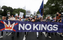 a group of people march down a street holding a banner that says " no kings "