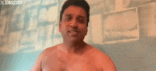 a shirtless man is standing in front of a brick wall and smiling for the camera .