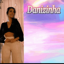 a woman in a black top and tan pants is smiling in front of a danizinha sign