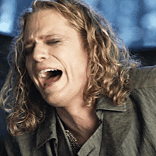 a man with long curly hair is crying with his mouth wide open