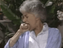 a woman with gray hair and a blue sweater is sitting outside with her hand to her mouth .