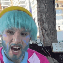 a man with blue hair and a beard is wearing a yellow hat