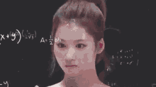 a woman with a ponytail is standing in front of a blackboard with a drawing of a triangle on her head .