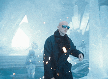 a bald man wearing sunglasses and a black coat stands in a snowy cave