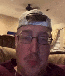 a man wearing a hat and glasses is sitting on a couch