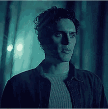 a man with curly hair is standing in a dark room in a blue light .