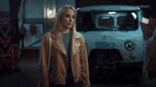 a woman in a brown jacket is standing in front of a white van .