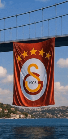 a large red white and yellow flag with 1905 on it hangs from a bridge over a body of water