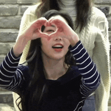 a woman making a heart with her hands in front of her eyes