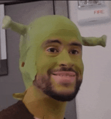 a man wearing a shrek mask is smiling in front of a fire extinguisher