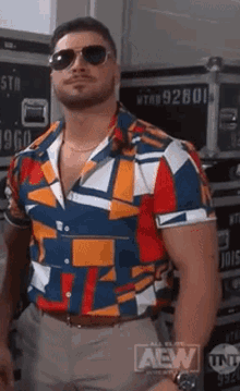 a man wearing sunglasses and a colorful shirt with a aew logo on the bottom